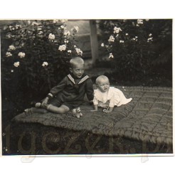 Małe dzieci na pikowanej narzucie siedzące na trawie wśród białych kwiatów