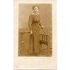 Dystyngowana dama stojąca przy bardzo stylowych meblach: fotelu Art Deco oraz stoliku ludwikowskim