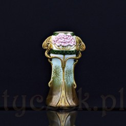 Ceramiczny wazon o smukłej formie, bogato dekorowany wypukłościami w masie, które przedstawiają kwiatostan bzu z listkami, które ukladają się w dwa uchwyty