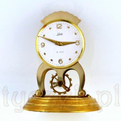 Niezwykły zegar w złotym kolorze pod szklaną kpułą