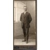 Dystyngowany, elegancko ubrany mężczyzna stojący przy uchylonym oknie na dawnym zdjęciu